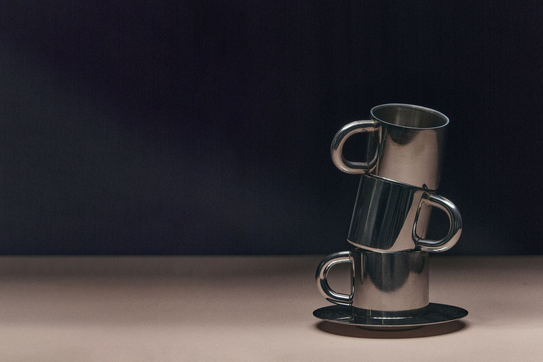 Three reflective metal cups stacked against a dark blue background